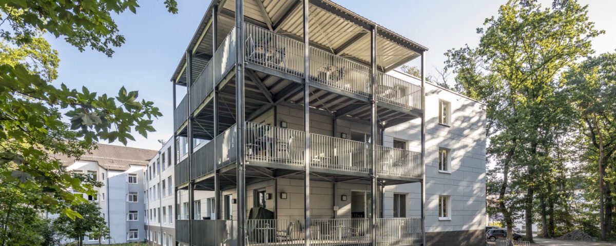 Mehrstöckiges Wohngebäude mit Balkonen im Grünen bei Sonnenschein, modernes Design.