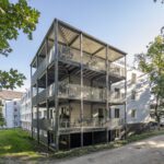 Mehrstöckiges Wohngebäude mit Balkonen im Grünen bei Sonnenschein, modernes Design.