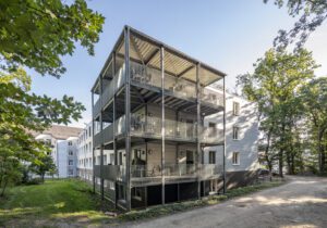 Mehrstöckiges Wohngebäude mit Balkonen im Grünen bei Sonnenschein, modernes Design.