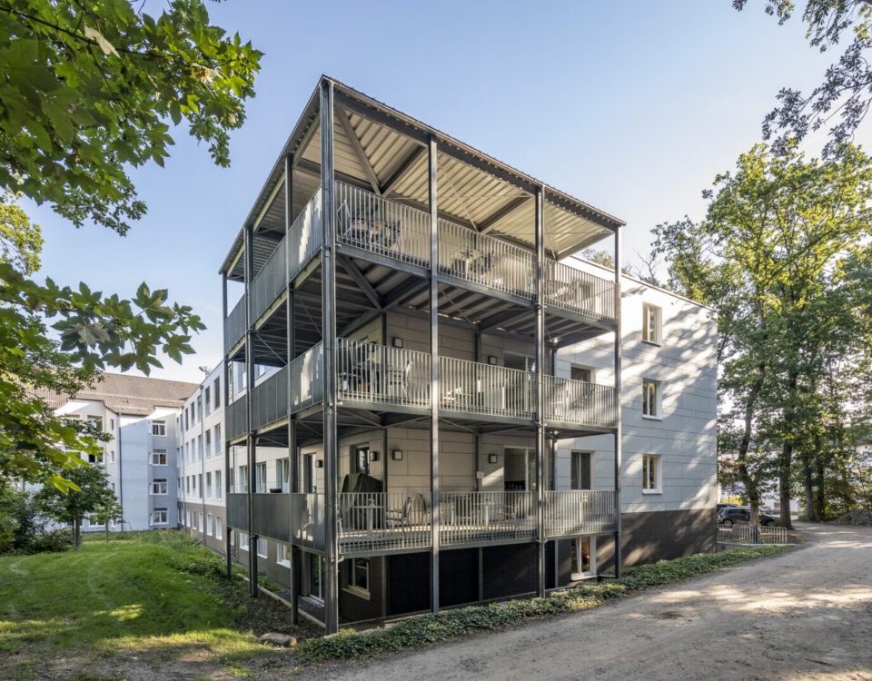 Mehrstöckiges Wohngebäude mit Balkonen im Grünen bei Sonnenschein, modernes Design.