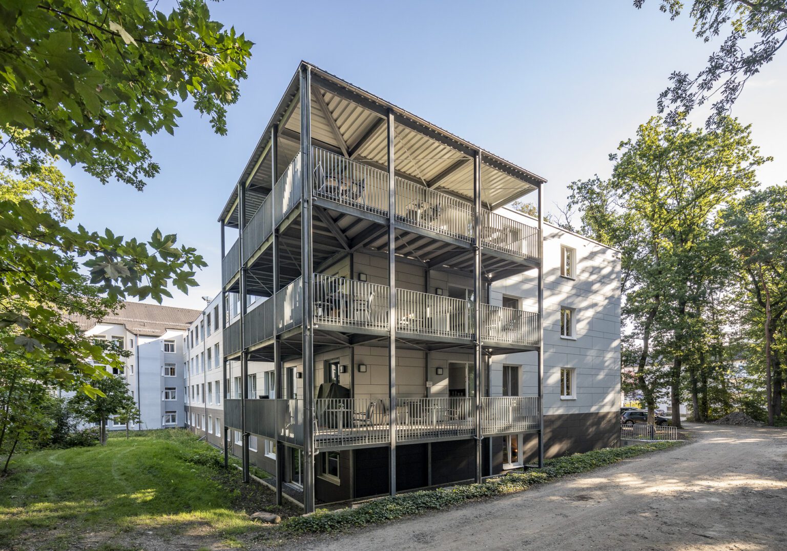 Mehrstöckiges Wohngebäude mit Balkonen im Grünen bei Sonnenschein, modernes Design.