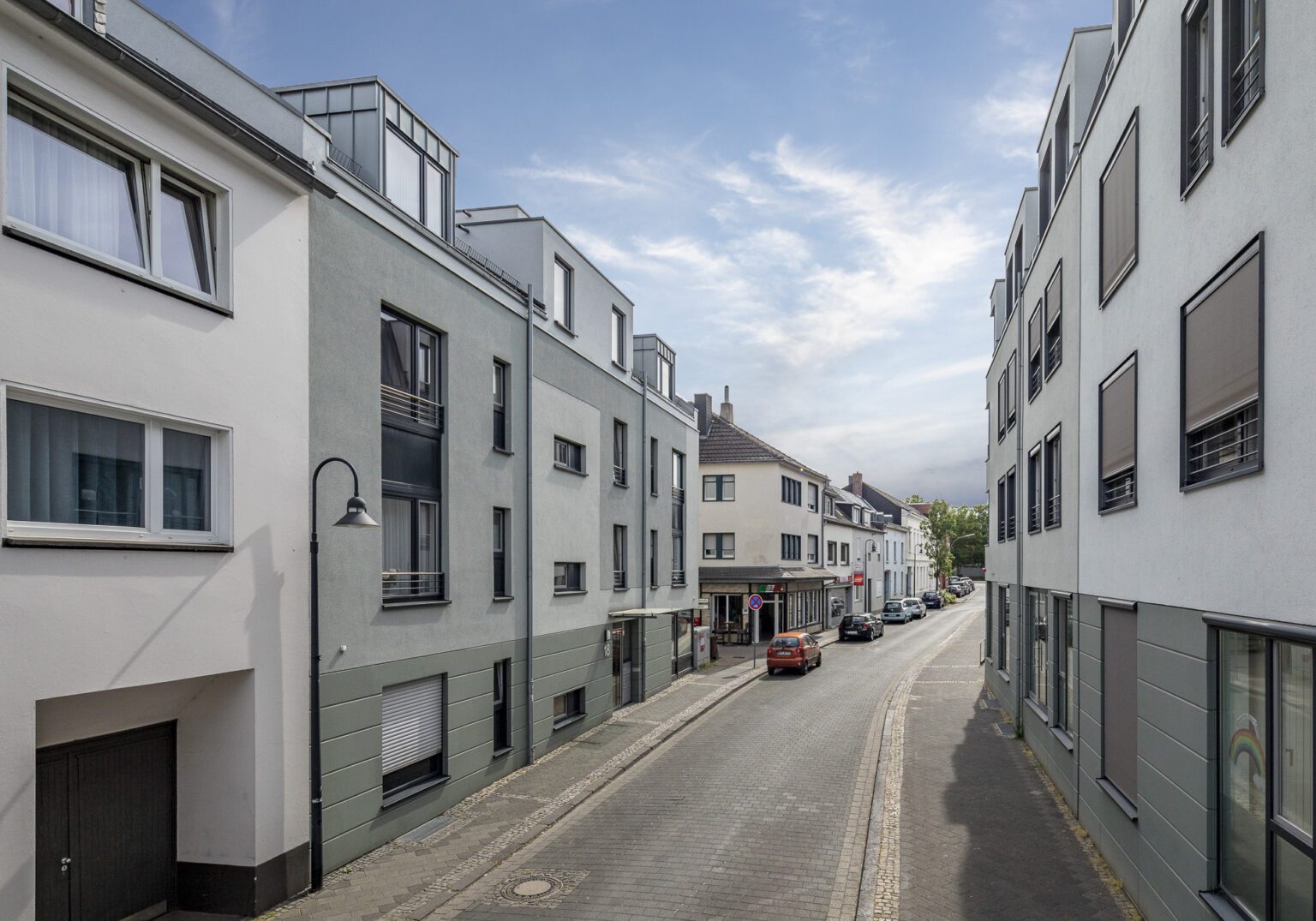 Moderne deutsche Wohnstraße mit mehrstöckigen Gebäuden, geparkten Autos und leicht bewölktem Himmel.