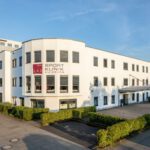Weiße Sportklinik Duisburg in sonniger Umgebung mit grünem Eingangsbereich und moderner Architektur.