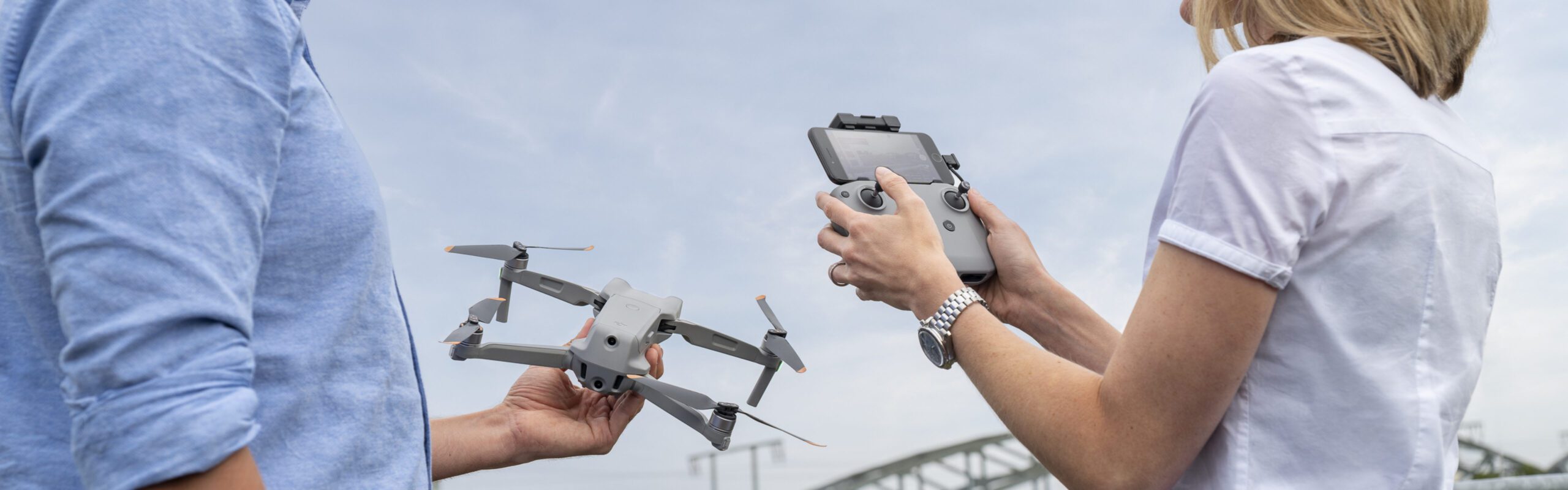 Zwei Personen steuern eine Drohne im Freien mit einer Fernsteuerung unter klarem Himmel.