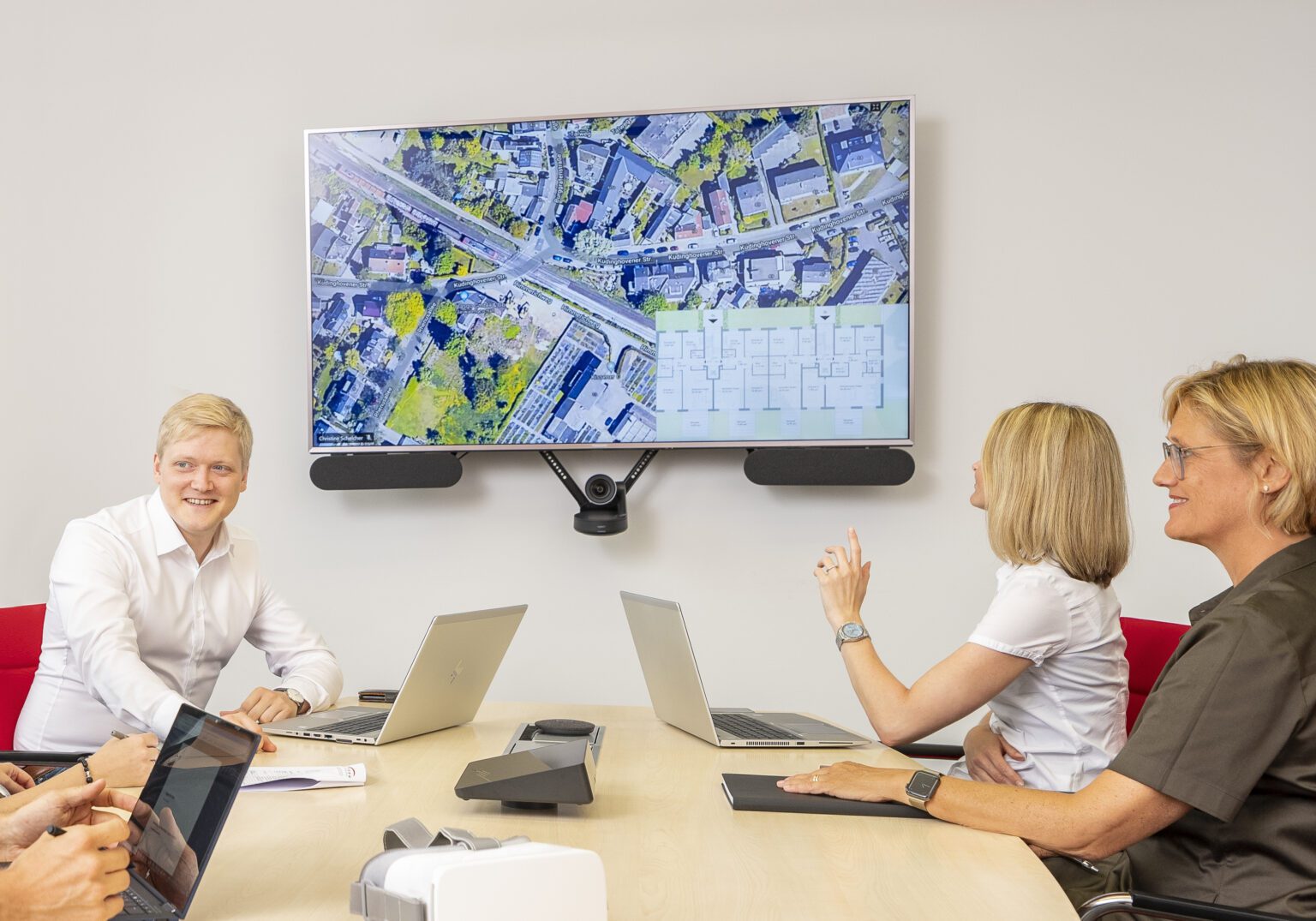 Moderne Bürokonferenz mit Laptop, Bildschirm mit Stadtkarte, diskutierende Personen, kollegiale Zusammenarbeit.