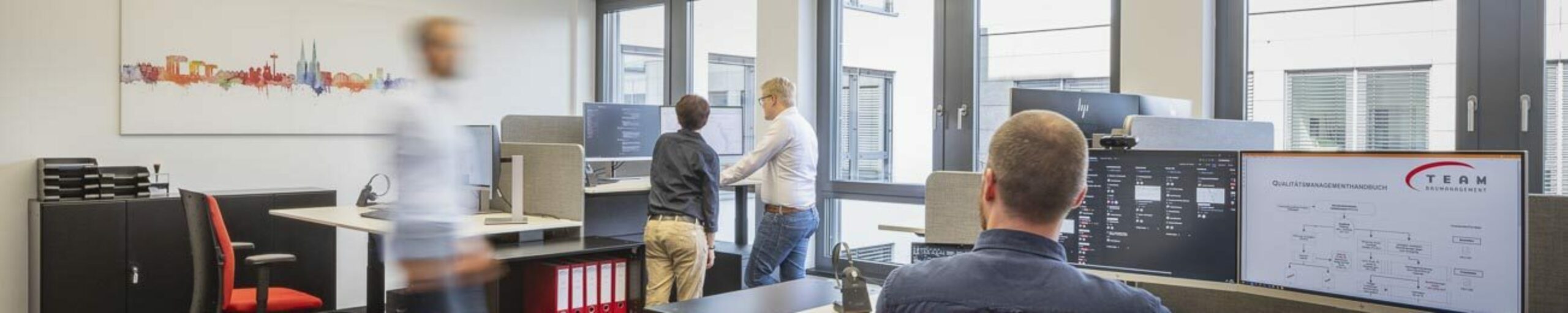 Modernes Büro mit Mitarbeitern, die an Computern arbeiten, und großer Fensterfront für viel natürliches Licht.