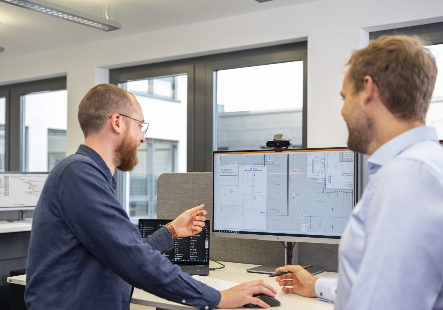 Zwei Männer arbeiten im Büro an einem Computer mit technischen Zeichnungen auf dem Bildschirm.