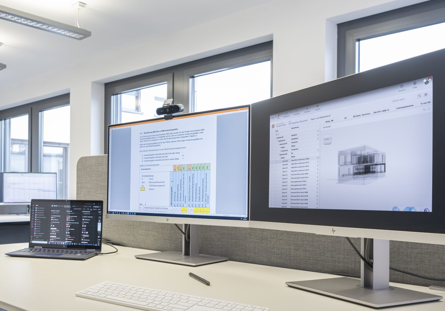 1717_047_AUSWAHL_12-Motiv_BIM-16x5-1-1536x1075.2-c-default Drei Computerbildschirme auf einem modernen Arbeitsplatz mit technischer Software und Diagrammen.