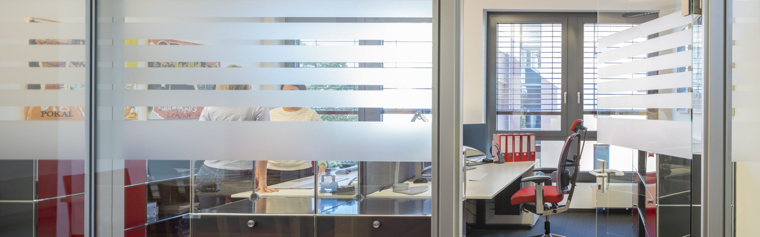 Moderne Bürofassaden mit Glaswänden, Sichtschutzstreifen und besetzten Schreibtischen für flexible Arbeitsumgebungen.