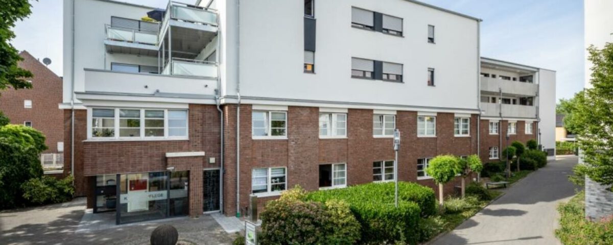 Moderne Wohnanlage mit roter Backsteinfassade und begrüntem Eingangsbereich unter blauem Himmel.