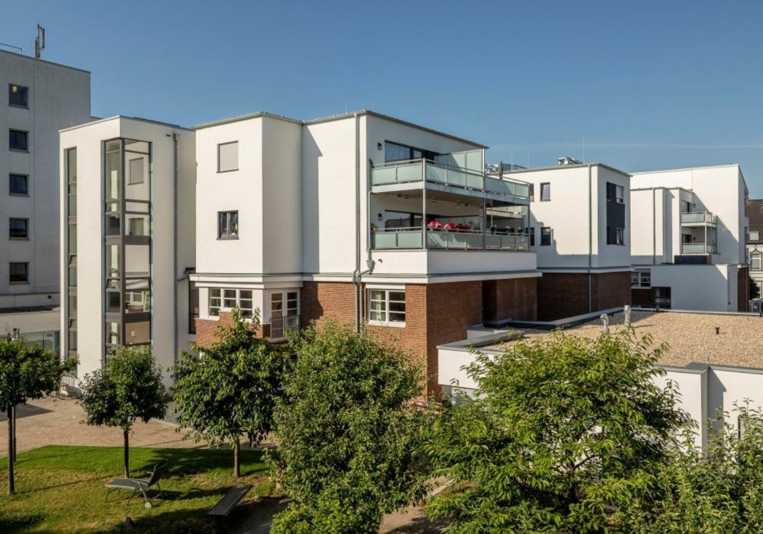 Moderne Wohnanlage mit Balkonen und Garten bei sonnigem Wetter.