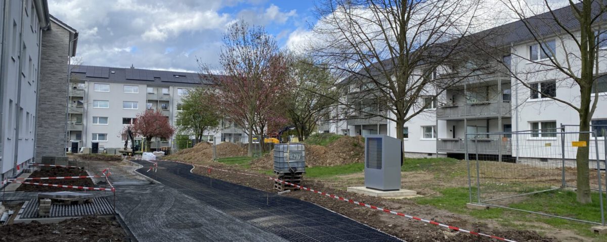 Baustelle in Wohnanlage mit neuen Gehwegen, Bauarbeiten im Freien bei bewölktem Himmel, Bäume ohne Laub.