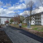 Baustelle in Wohnanlage mit neuen Gehwegen, Bauarbeiten im Freien bei bewölktem Himmel, Bäume ohne Laub.