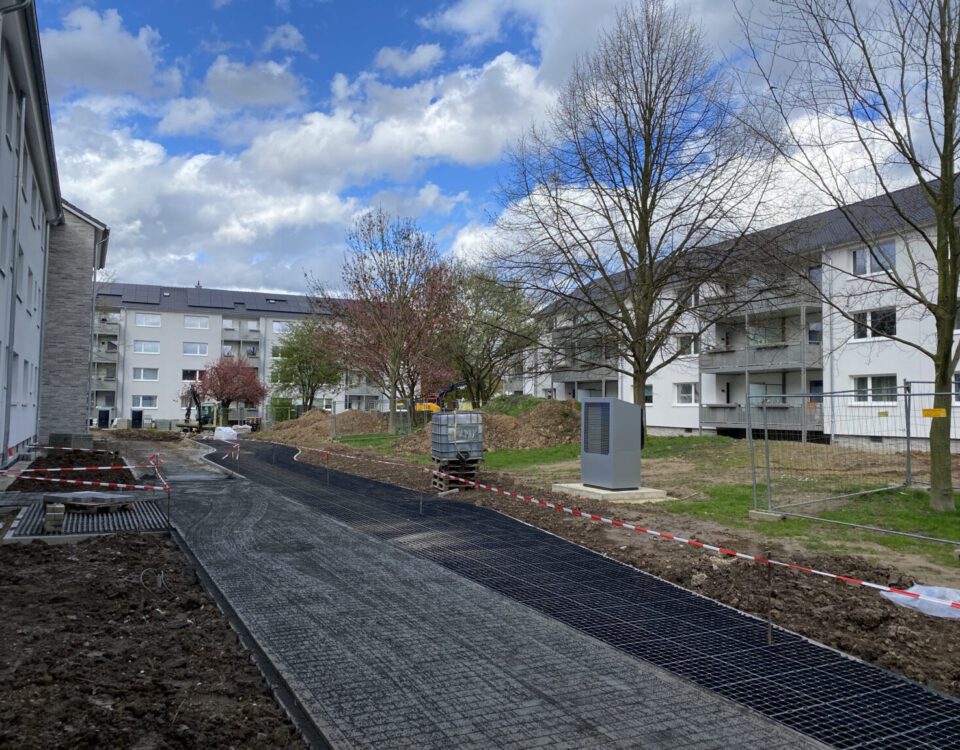 Baustelle in Wohnanlage mit neuen Gehwegen, Bauarbeiten im Freien bei bewölktem Himmel, Bäume ohne Laub.