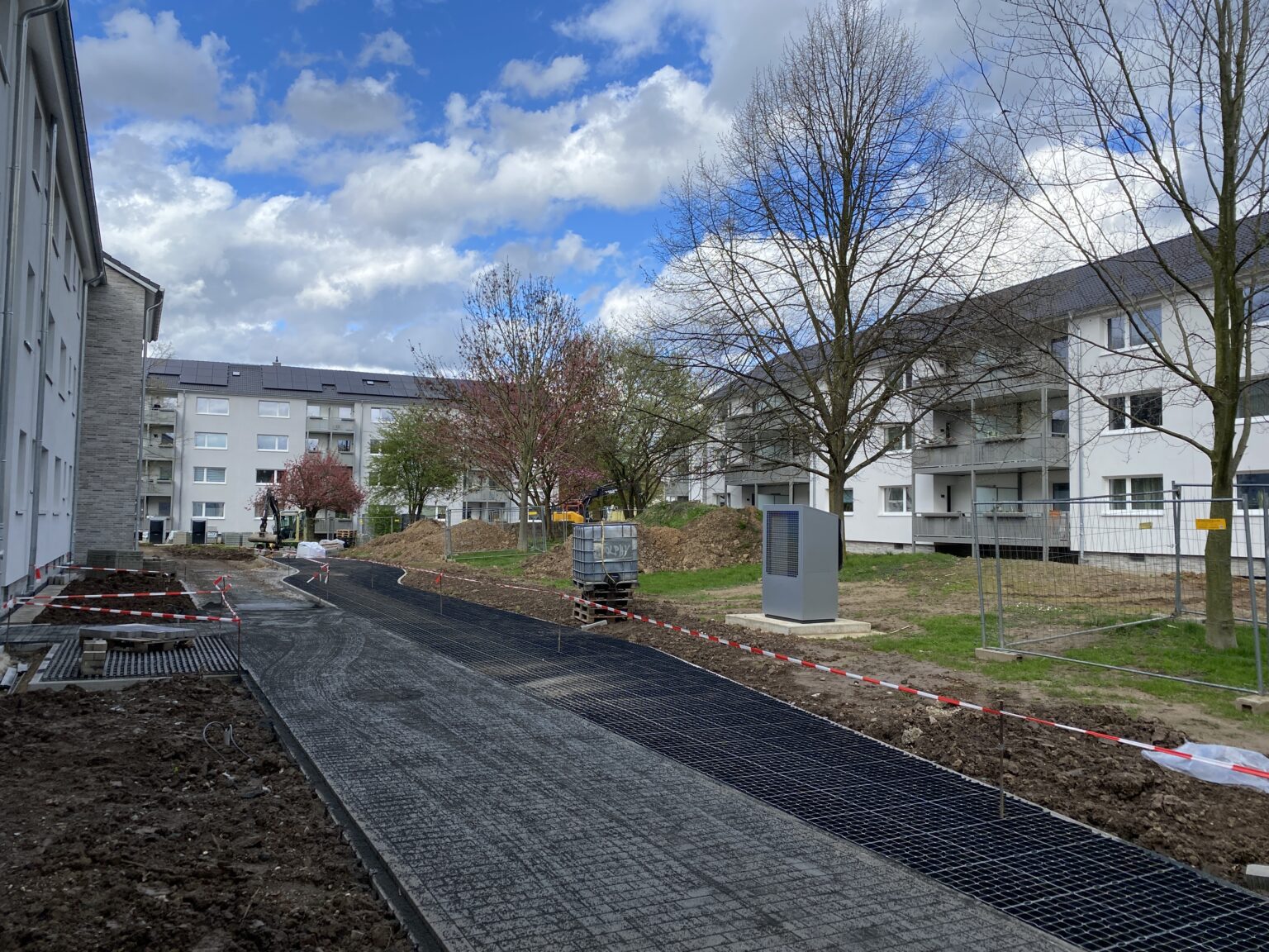 Baustelle in Wohnanlage mit neuen Gehwegen, Bauarbeiten im Freien bei bewölktem Himmel, Bäume ohne Laub.