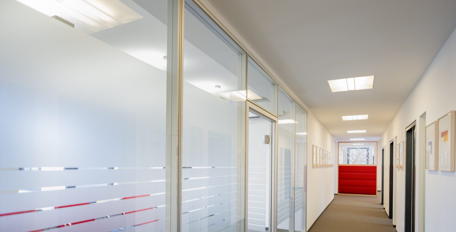 Moderner Büroflur mit Glaswänden und heller Beleuchtung, minimalistisches Design.