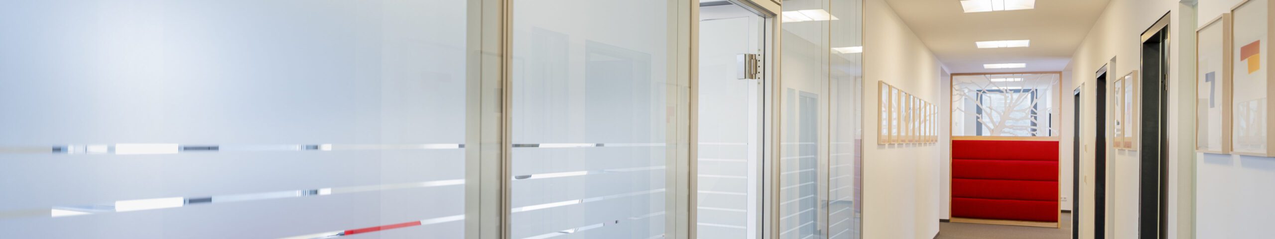 Moderne Büroeinrichtung: Helle Flure mit Glastüren und roten Akzenten, schafft eine offene und professionelle Arbeitsumgebung.