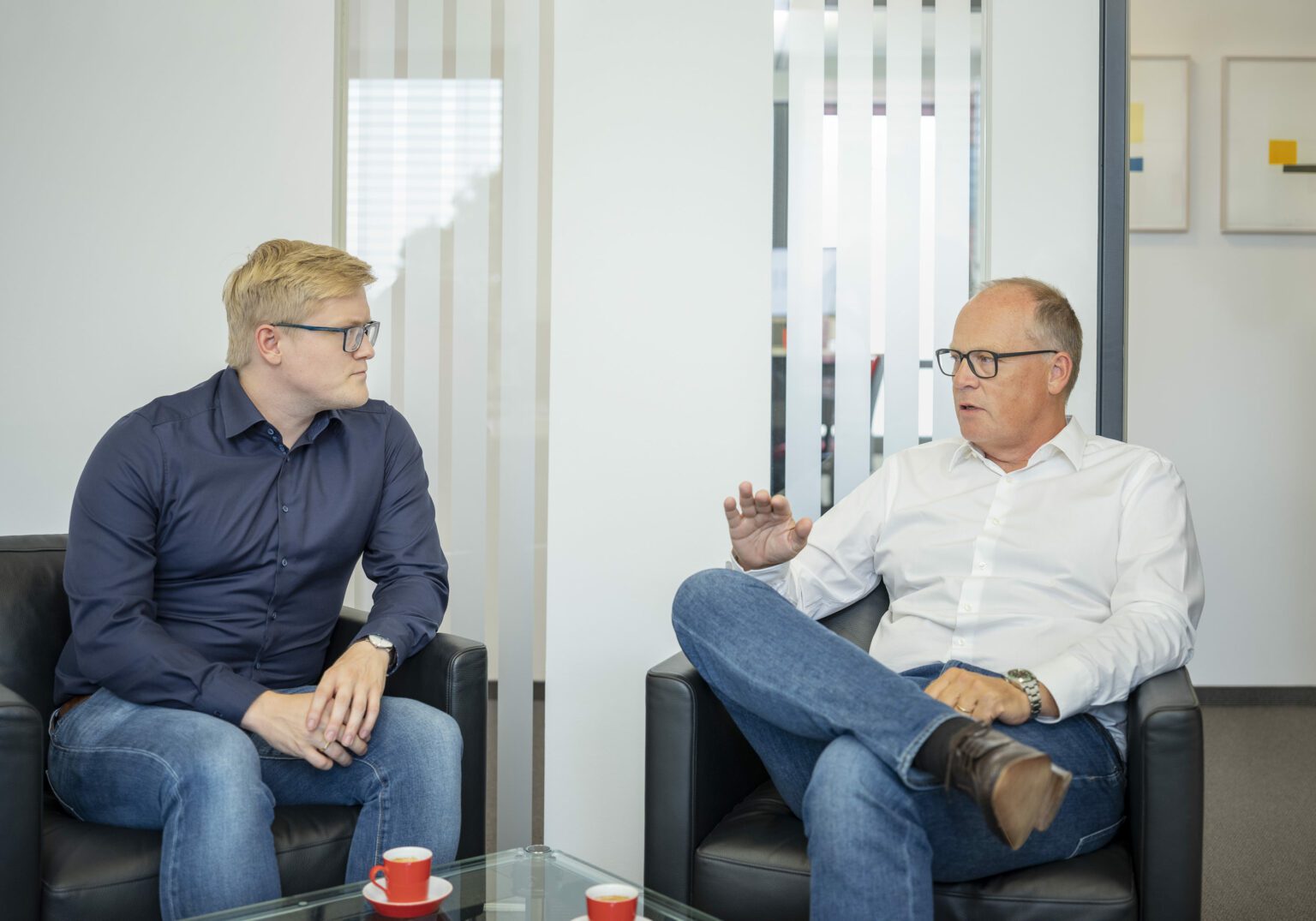 Zwei Männer im Gespräch in einem modernen Büro, mit Kaffeetassen auf dem Tisch.
