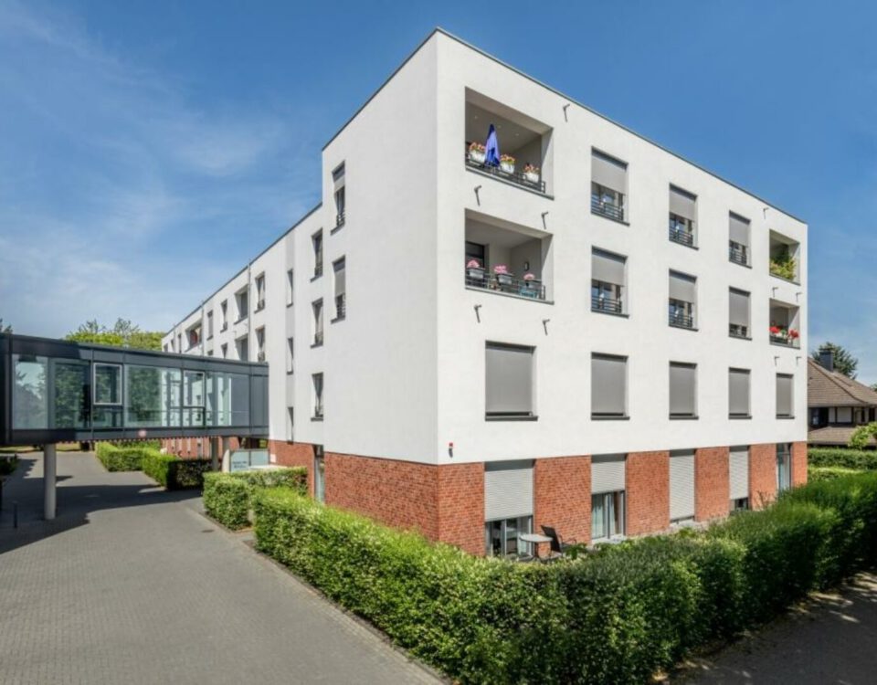 Moderne Wohnanlage mit weißen Fassaden und Balkonen an einem sonnigen Tag, umgeben von gepflegten Hecken.