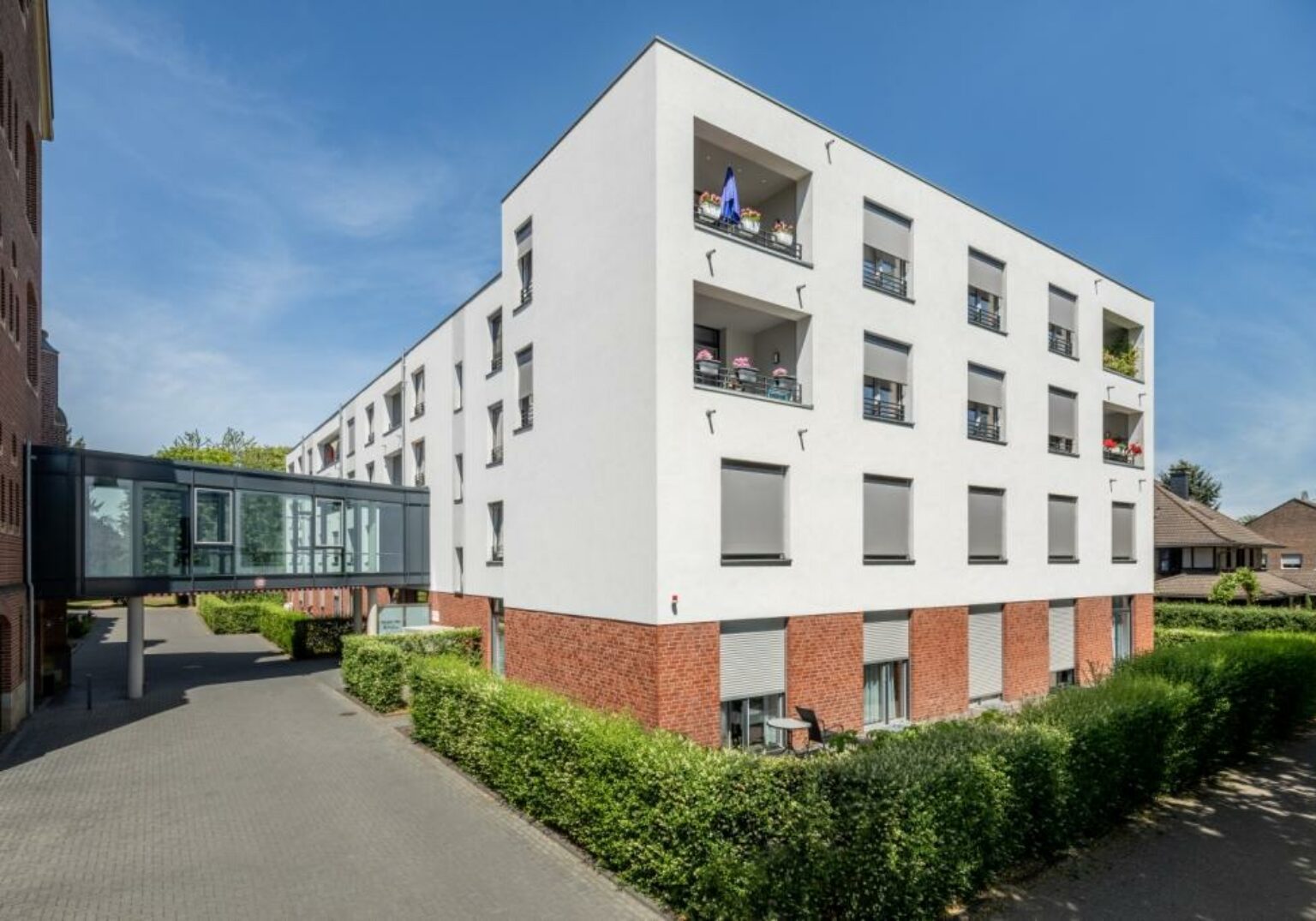 Moderne Wohnanlage mit weißen Fassaden und Balkonen an einem sonnigen Tag, umgeben von gepflegten Hecken.