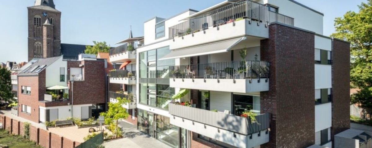 Moderne Wohnanlage mit Balkonen und historischer Kirche im Hintergrund.