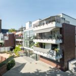 Moderne Wohnanlage mit Balkonen und historischer Kirche im Hintergrund.