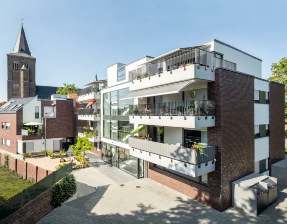 Moderne Wohnanlage mit Balkonen und historischer Kirche im Hintergrund.