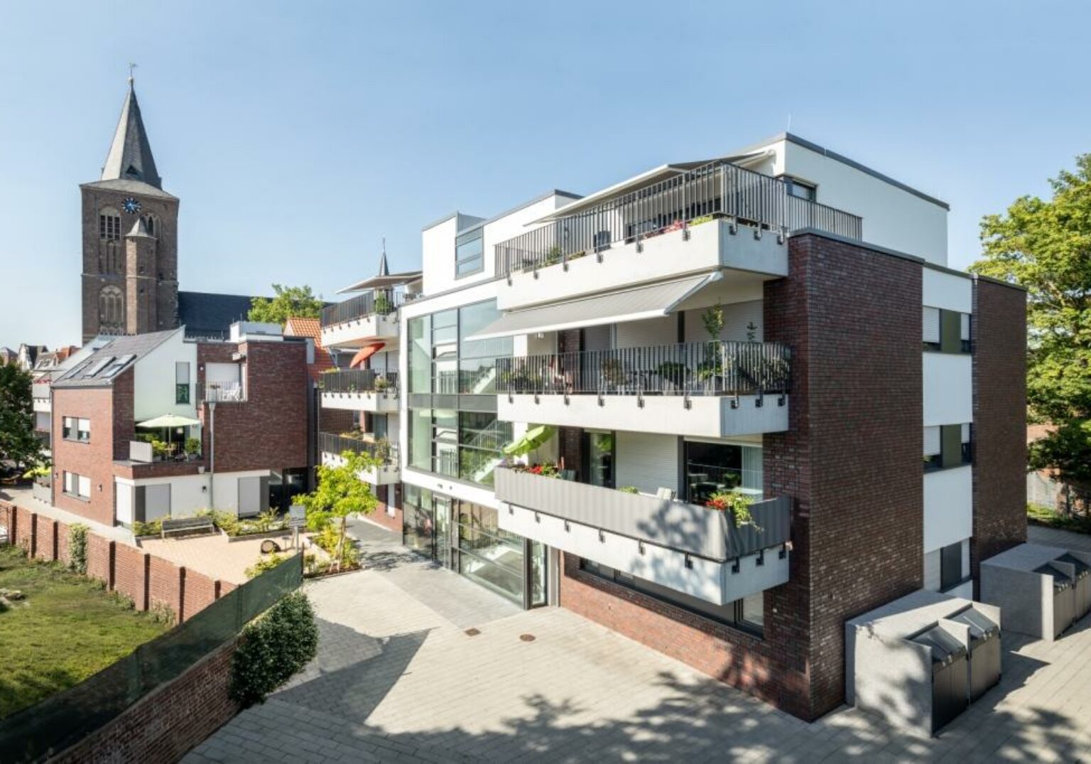 Moderne Wohnanlage mit Balkonen und historischer Kirche im Hintergrund.