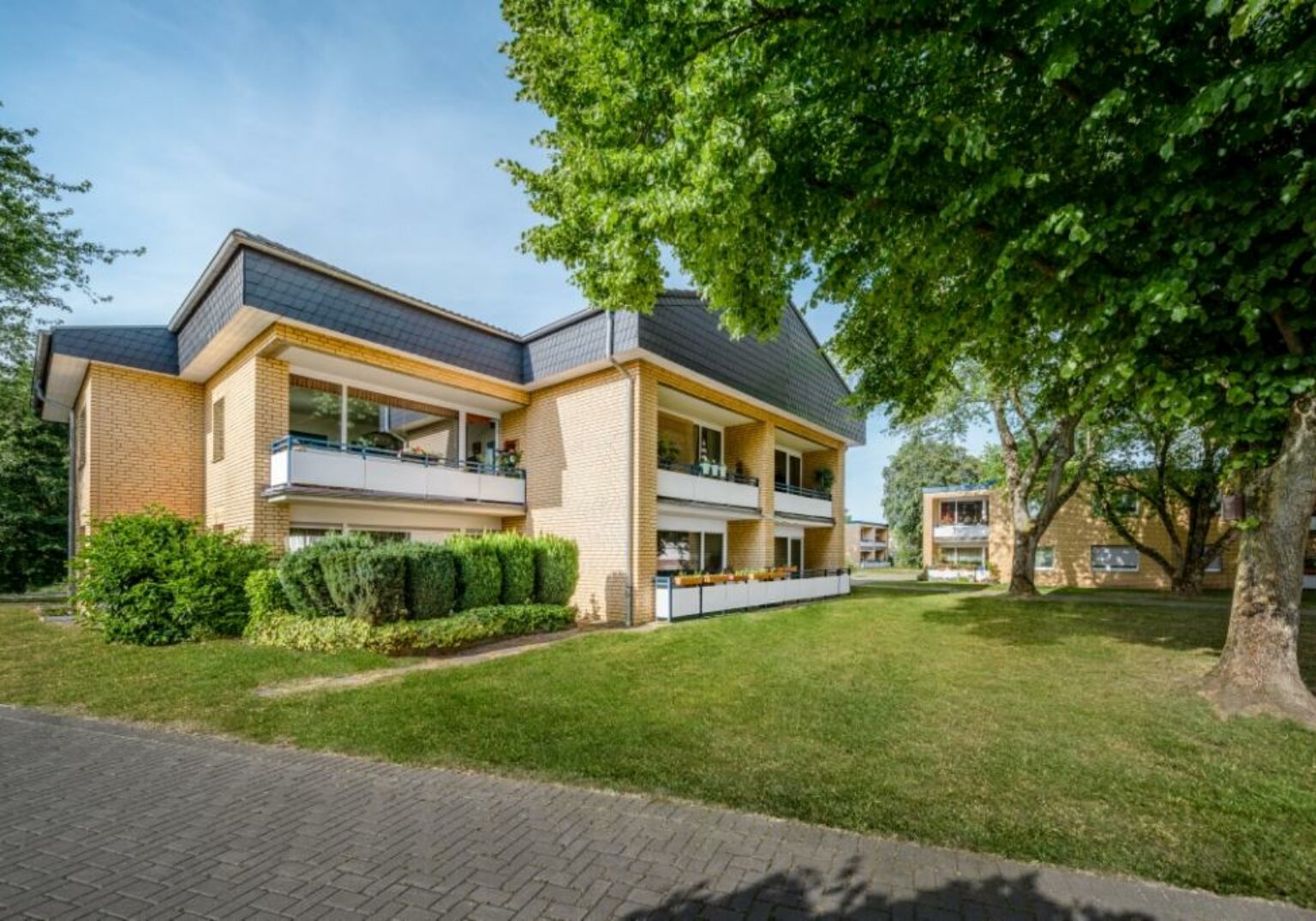 Moderner Wohnkomplex im Grünen mit Balkonen, Backstein-Fassade und gepflegter Gartenanlage, ideal für urbanes Wohnen.
