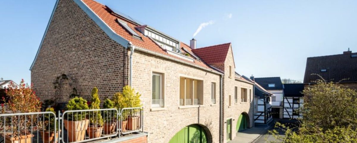 Modernes Backsteinhaus mit roten Dächern und grünen Toren in sonniger Wohngegend. Harmonische Architektur und Natur.