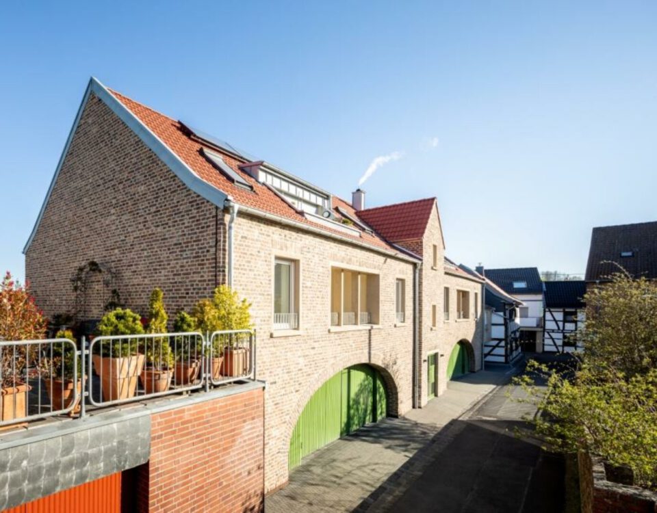 Modernes Backsteinhaus mit roten Dächern und grünen Toren in sonniger Wohngegend. Harmonische Architektur und Natur.