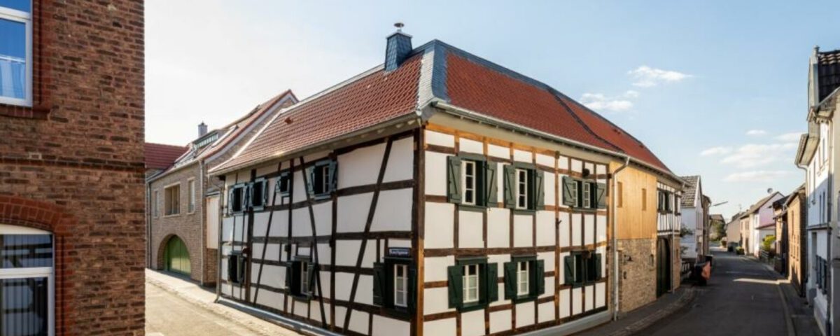 Fachwerkhaus an sonniger Straßenecke, typisch deutsches Architekturbeispiel mit roten Dächern und blauen Himmel.