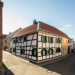 Fachwerkhaus an sonniger Straßenecke, typisch deutsches Architekturbeispiel mit roten Dächern und blauen Himmel.