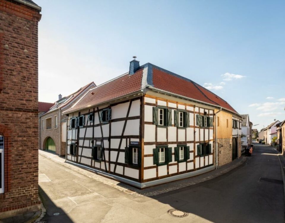 Fachwerkhaus an sonniger Straßenecke, typisch deutsches Architekturbeispiel mit roten Dächern und blauen Himmel.