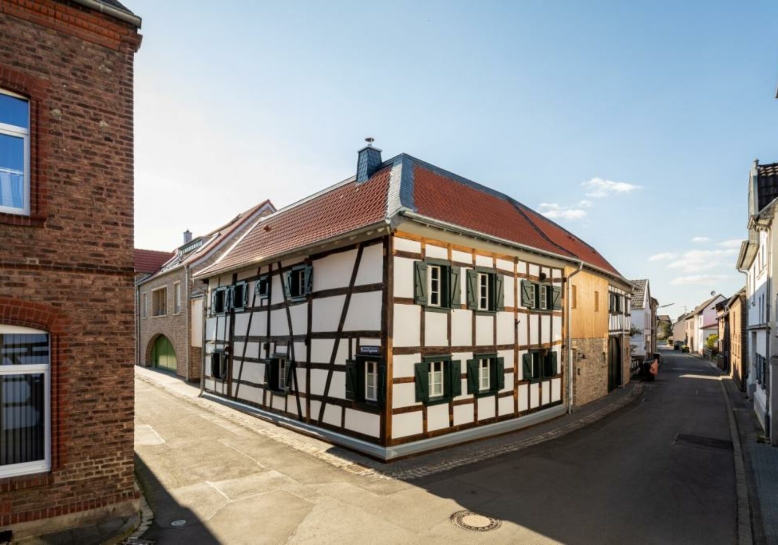 Fachwerkhaus an sonniger Straßenecke, typisch deutsches Architekturbeispiel mit roten Dächern und blauen Himmel.