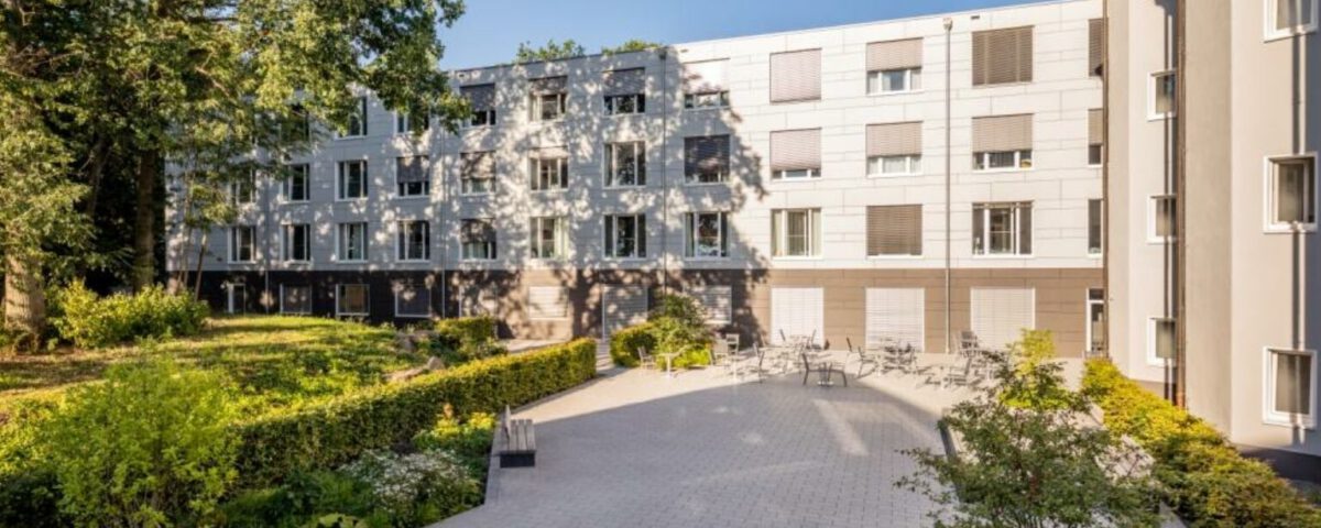 Wohngebäude mit moderner Fassade und grünem Innenhof an einem sonnigen Tag, ideal für urbanes Wohnen.
