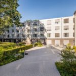 Wohngebäude mit moderner Fassade und grünem Innenhof an einem sonnigen Tag, ideal für urbanes Wohnen.