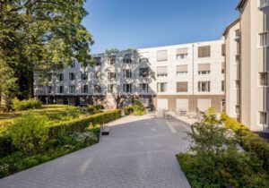 Wohngebäude mit moderner Fassade und grünem Innenhof an einem sonnigen Tag, ideal für urbanes Wohnen.