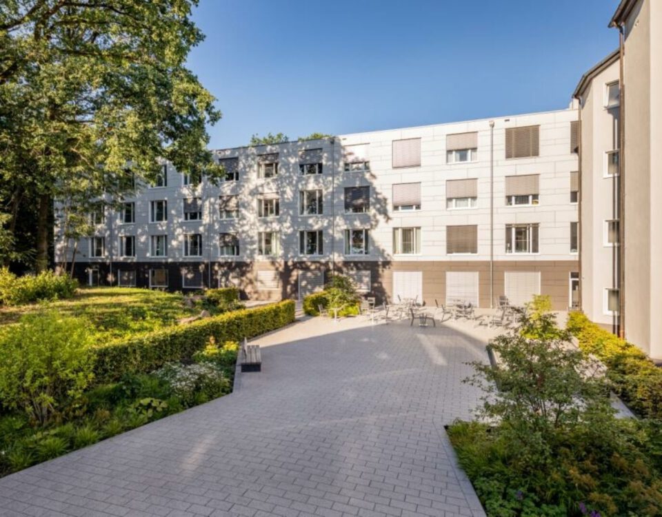 Wohngebäude mit moderner Fassade und grünem Innenhof an einem sonnigen Tag, ideal für urbanes Wohnen.