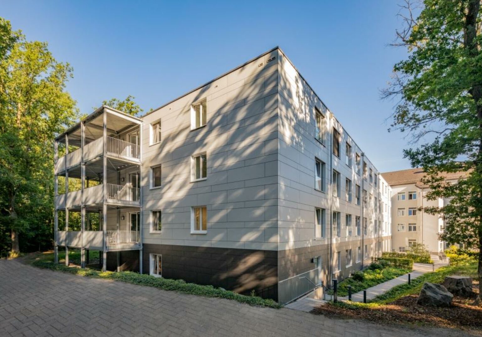 Moderne Wohnanlage mit Balkonen, umgeben von Bäumen, unter blauem Himmel. Ideal für urbanes Leben und Naturgenuss.