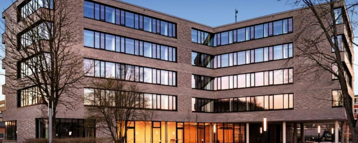 Moderne Bürogebäude-Fassade bei Sonnenuntergang mit großen Glasfenstern und blauer Himmel im Hintergrund.
