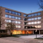 Moderne Bürogebäude-Fassade bei Sonnenuntergang mit großen Glasfenstern und blauer Himmel im Hintergrund.