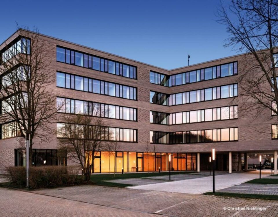 Moderne Bürogebäude-Fassade bei Sonnenuntergang mit großen Glasfenstern und blauer Himmel im Hintergrund.