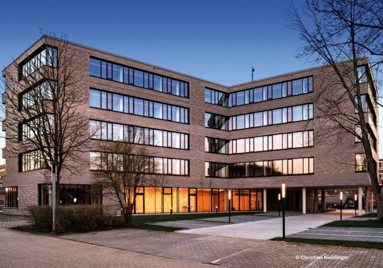 Moderne Bürogebäude-Fassade bei Sonnenuntergang mit großen Glasfenstern und blauer Himmel im Hintergrund.