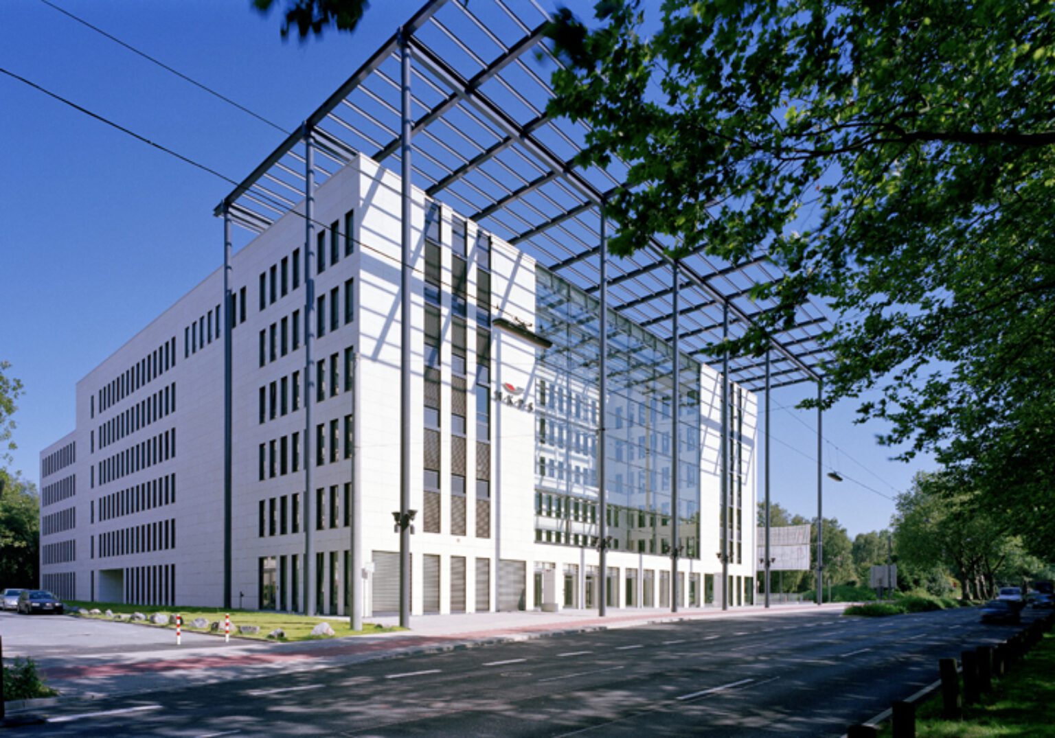 Modernes Bürogebäude mit Glasfassade und umliegender grüner Landschaft, unter blauem Himmel.