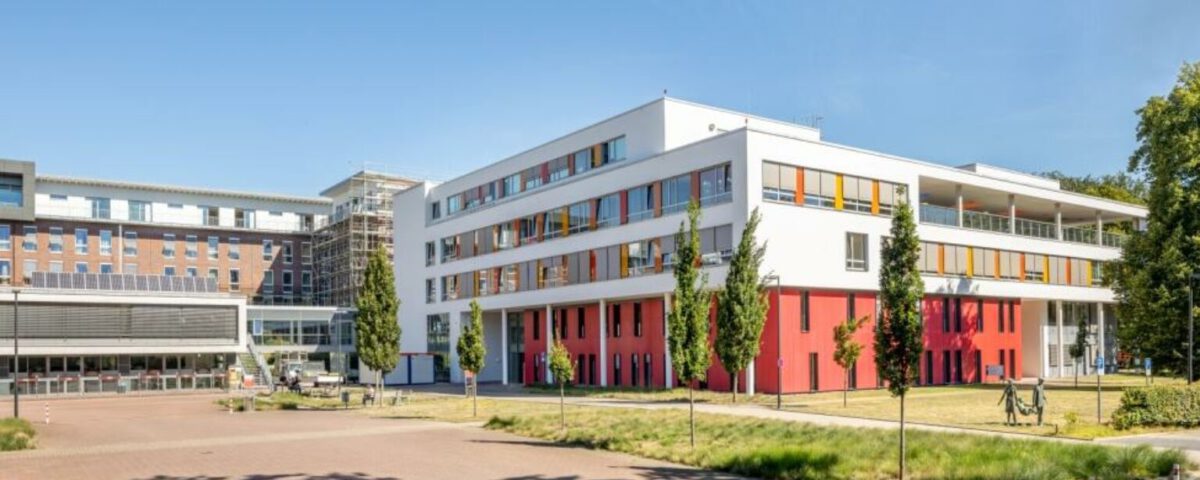Modernes Gebäude mit bunten Akzenten, umgeben von Bäumen, unter blauem Himmel. Ideal für Urbanität und Architekturstudien.