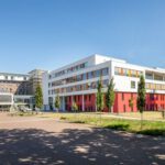 Modernes Gebäude mit bunten Akzenten, umgeben von Bäumen, unter blauem Himmel. Ideal für Urbanität und Architekturstudien.