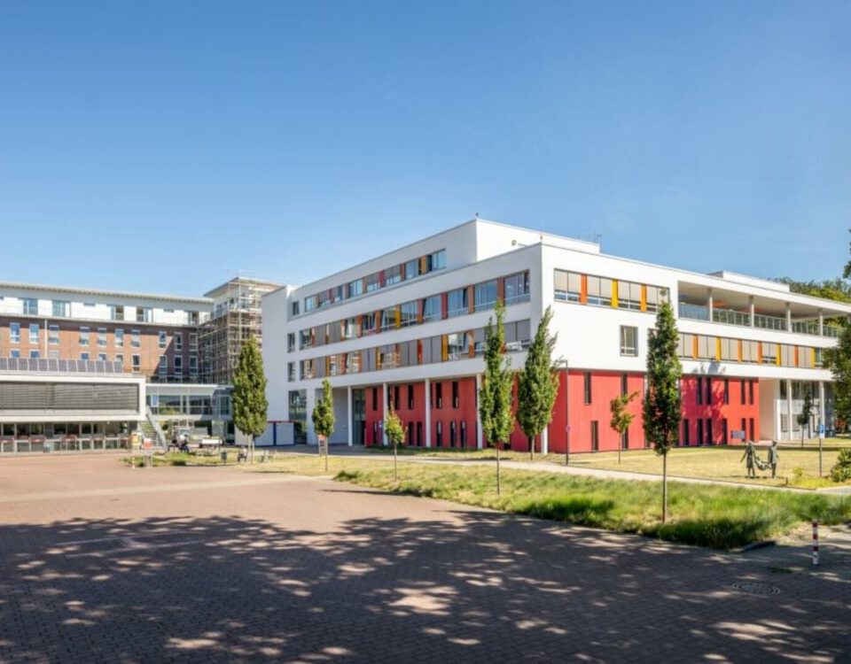 Modernes Gebäude mit bunten Akzenten, umgeben von Bäumen, unter blauem Himmel. Ideal für Urbanität und Architekturstudien.