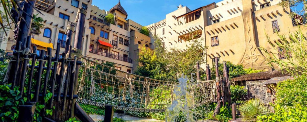 Afrika-inspiriertes Hotel mit Hängebrücke und Wasserfall im sonnigen grünen Garten, perfekter Urlaubsort für Familien.