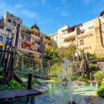 Afrika-inspiriertes Hotel mit Hängebrücke und Wasserfall im sonnigen grünen Garten, perfekter Urlaubsort für Familien.